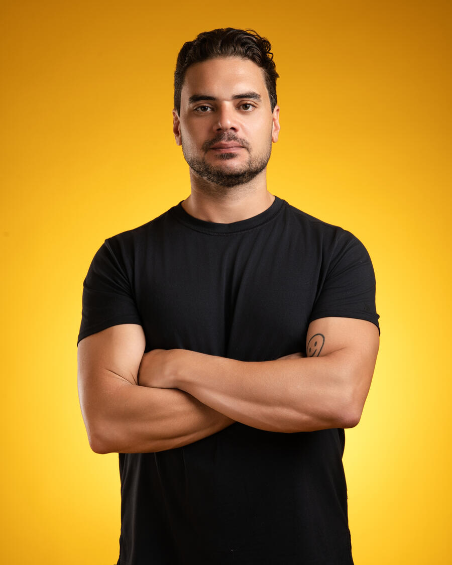 Portrait of Salim Heyaime, founder of Santosh Retreats, arms crossed in a black T-shirt against a warm yellow backdrop.
